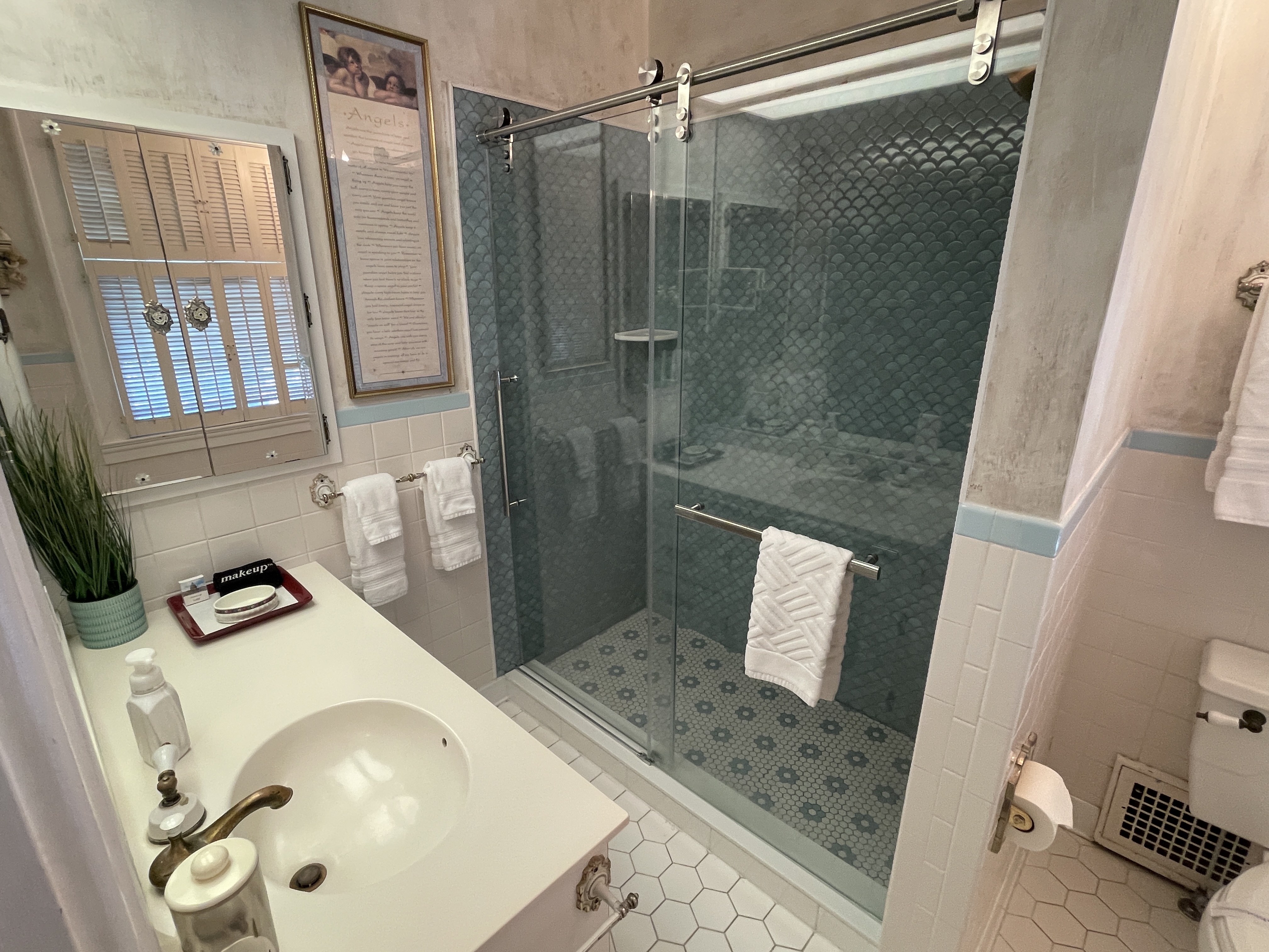 Modern bathroom featuring a stylish walk-in shower with geometric tiles. A clean vanity, fresh towels, and a touch of greenery complete the space.