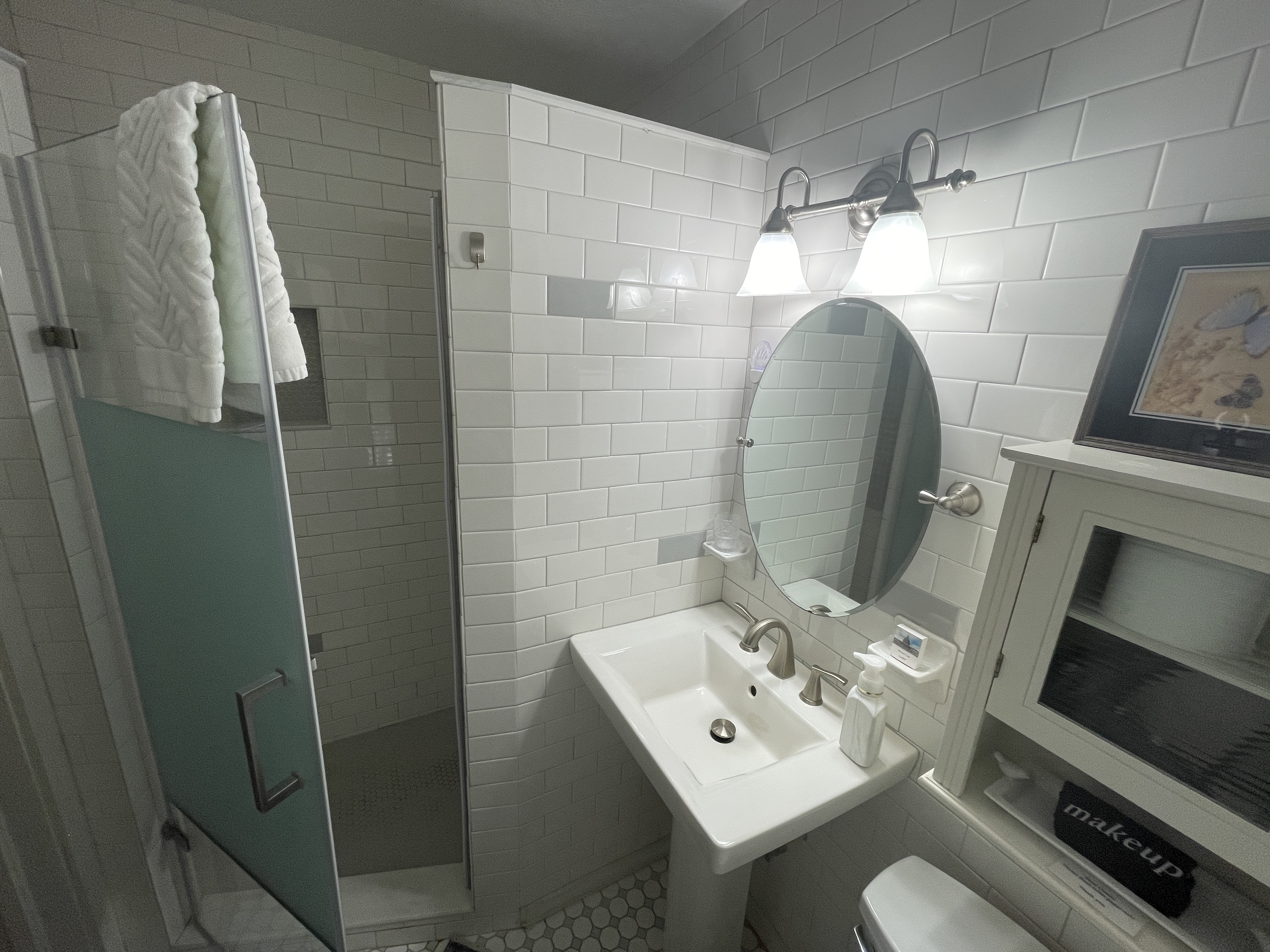 Bright and clean bathroom featuring a stylish walk-in shower with subway tiles. A classic pedestal sink and ample white towels create a fresh space.