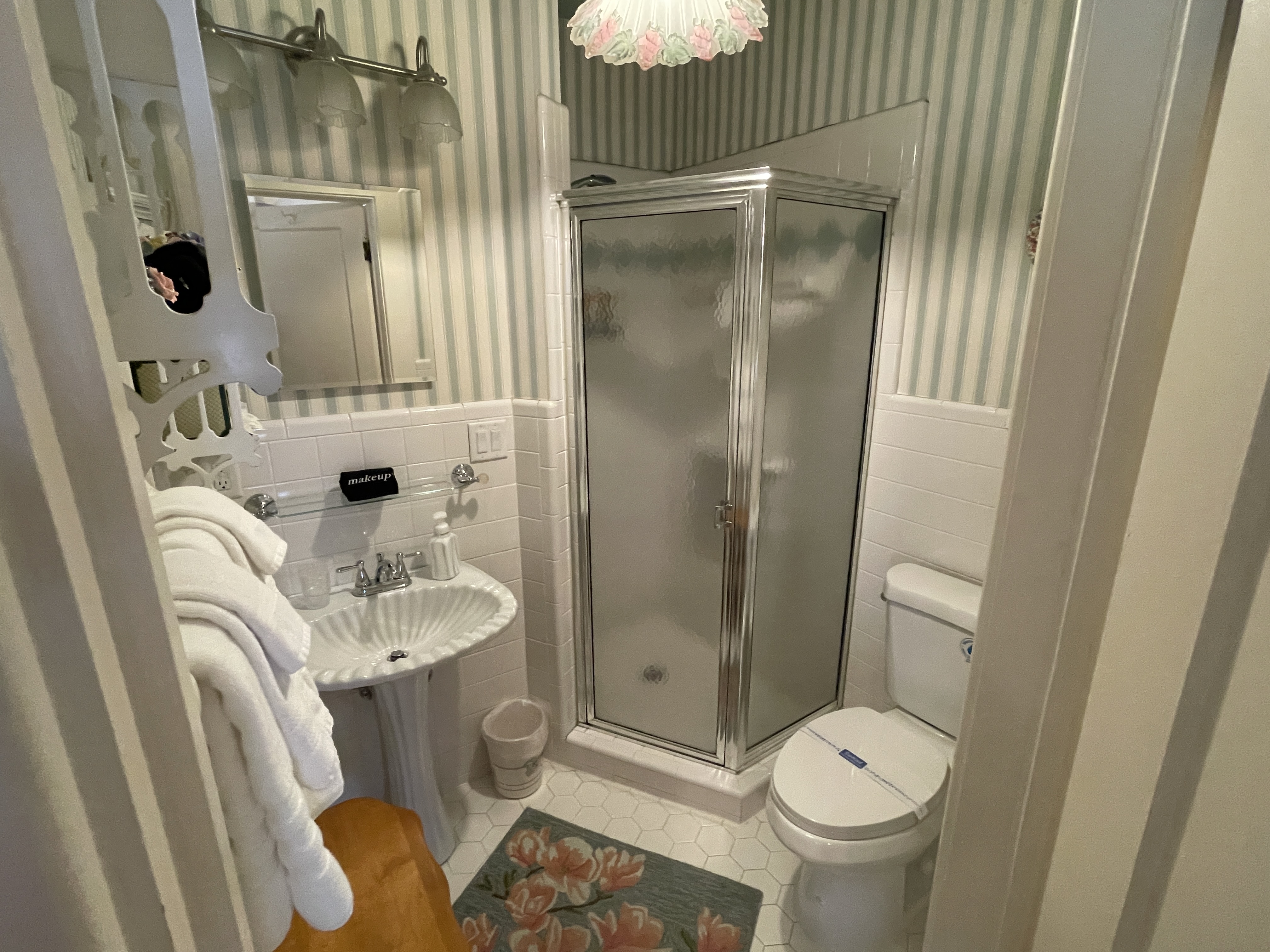 Cozy bathroom with classic striped wallpaper, a compact corner shower, and a pedestal sink.