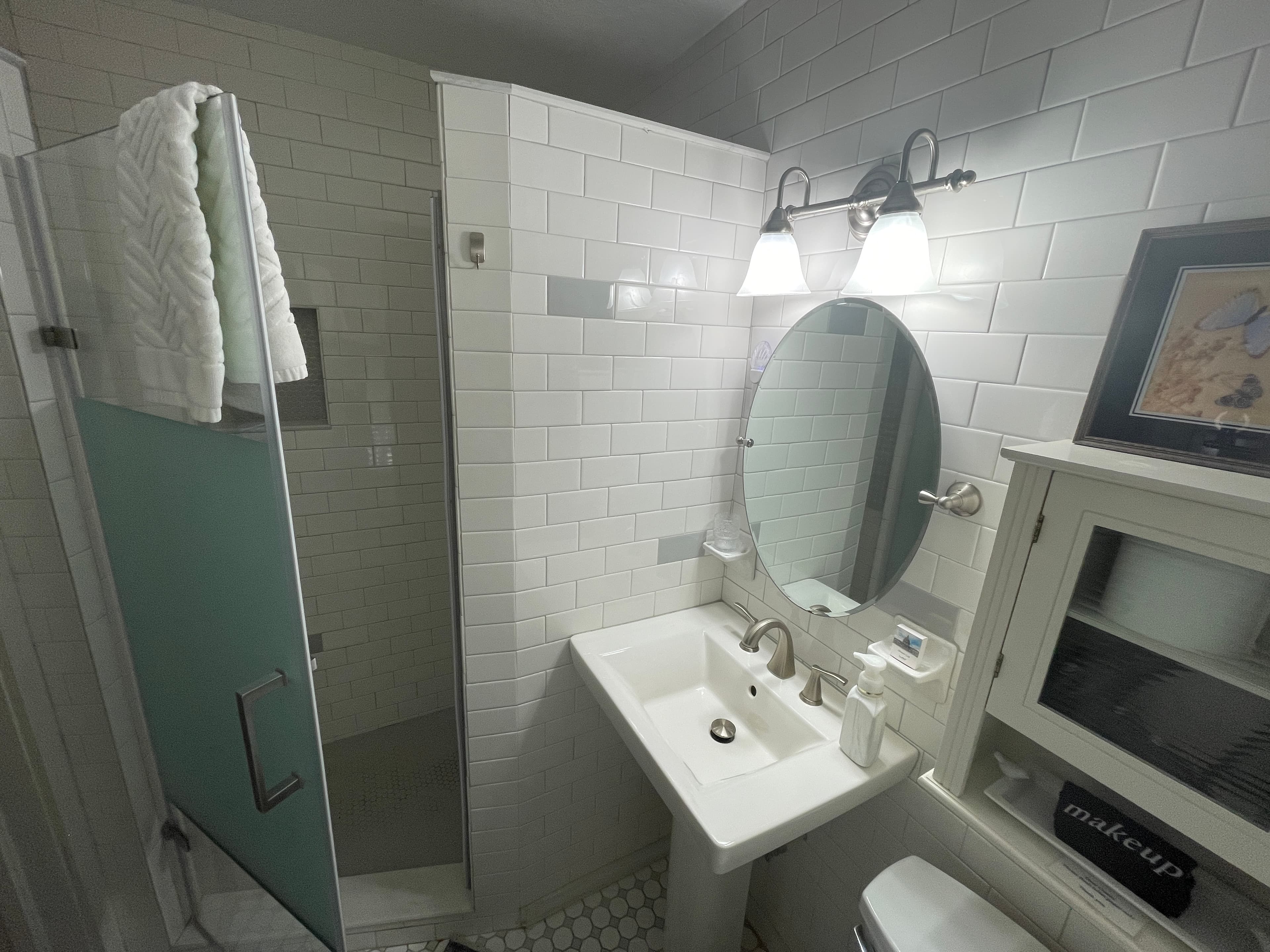 Bright and clean bathroom featuring a stylish walk-in shower with subway tiles. A classic pedestal sink and ample white towels create a fresh space.