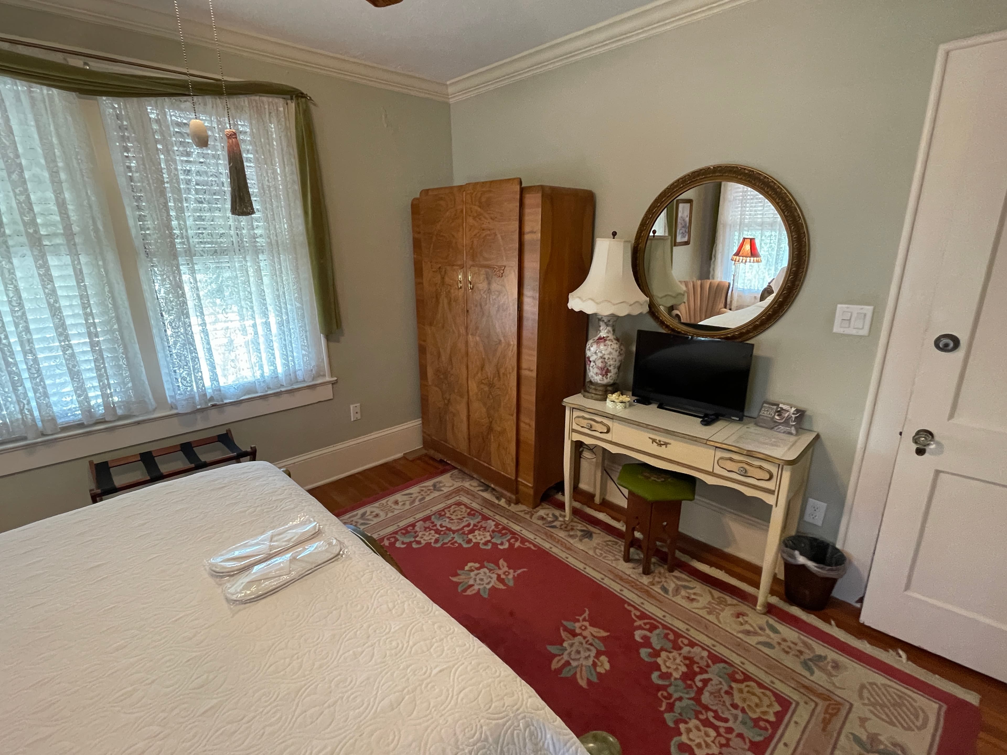 Charming bedroom with vintage wooden furniture, a cozy desk area, and a rich red rug. Soft lighting and classic decor create a peaceful and inviting space.