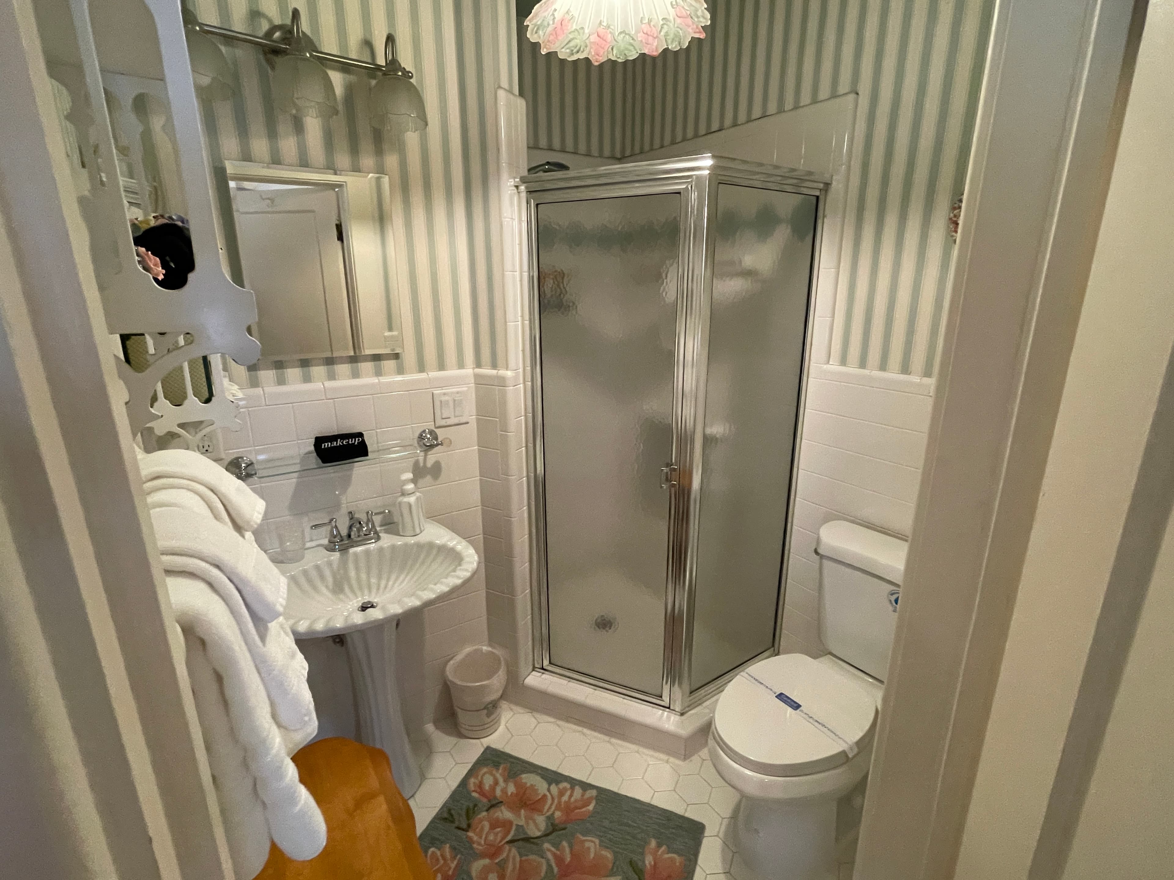 Cozy bathroom with classic striped wallpaper, a compact corner shower, and a pedestal sink.