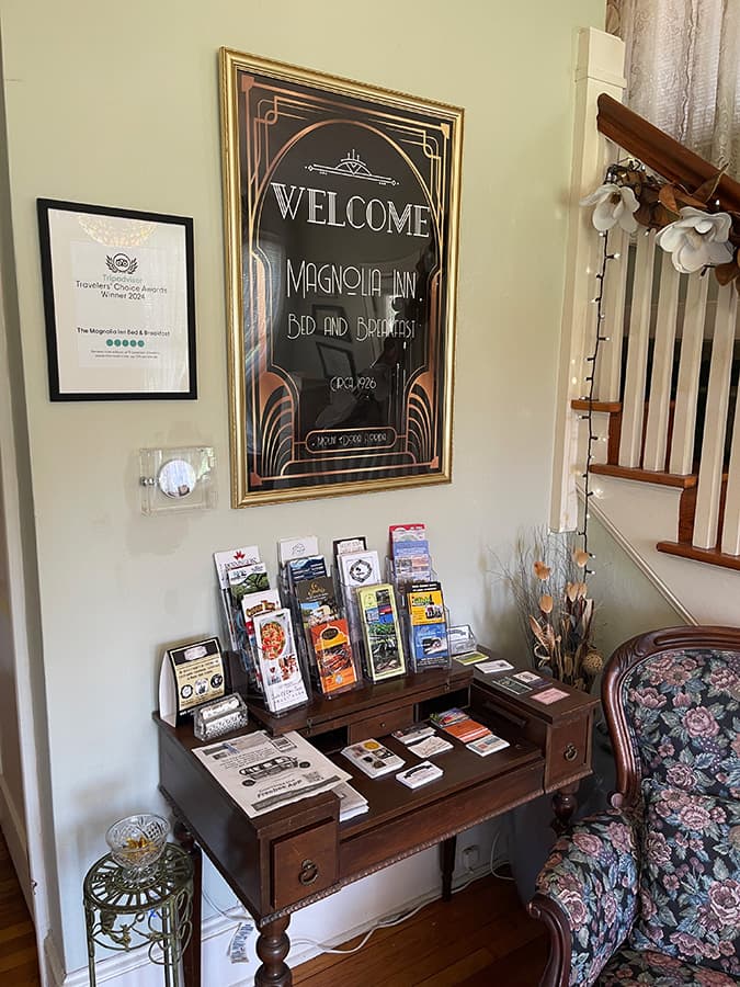 A welcoming interior of Magnolia Inn Bed and Breakfast, featuring a decorative sign and a wooden table displaying brochures and information.