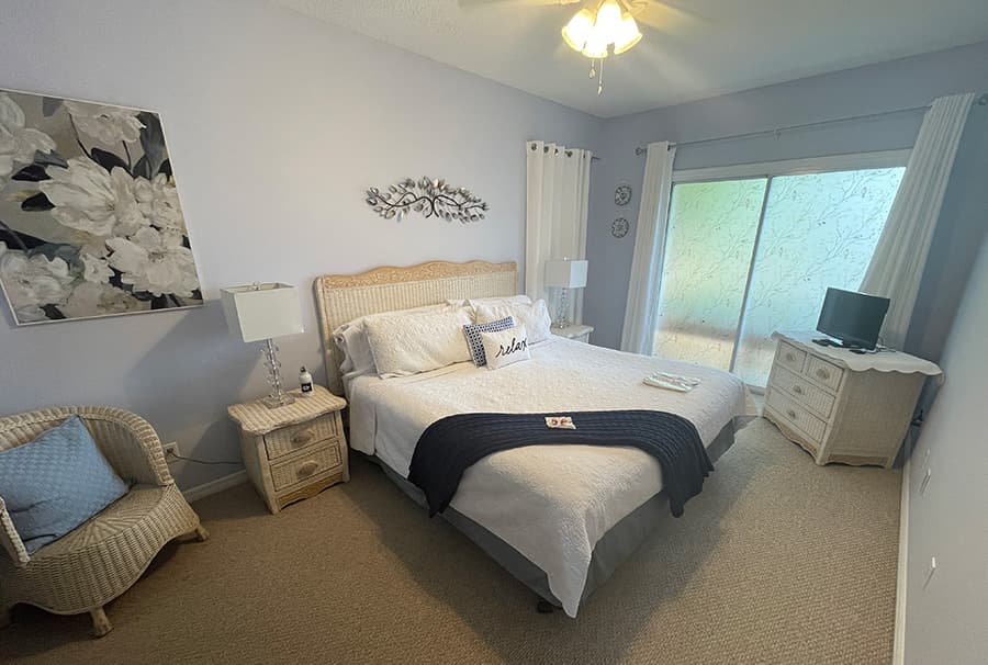 Cozy bedroom featuring a queen-sized bed, wicker furniture, and a glass door leading to a balcony.